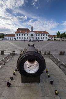 A large cannon displayed in a large square with buildings in the background, beneath a cloudy sky.