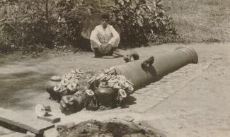 A man sits behind the Si Jagur cannon circa 1930. Offerings can be seen placed in front of the cannon