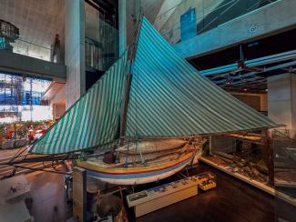 A traditional wooden sailboat with a green and white striped sail displayed in a museum.