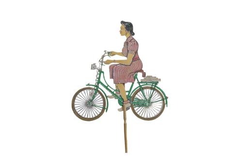 A leather puppet depicting a woman wearing a pink dress riding a green bike