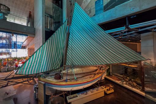 A traditional wooden sailboat with a green and white striped sail displayed in a museum.