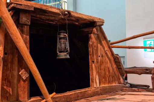 Closeup of a traditional wooden sailboat with a green and white striped sail displayed in a museum.