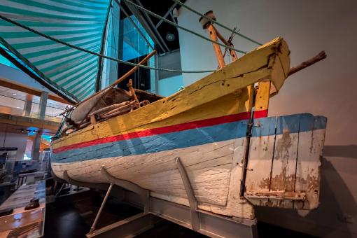 A traditional wooden sailboat with a green and white striped sail displayed in a museum.