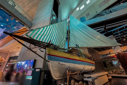 A traditional wooden sailboat with a green and white striped sail displayed in a museum.