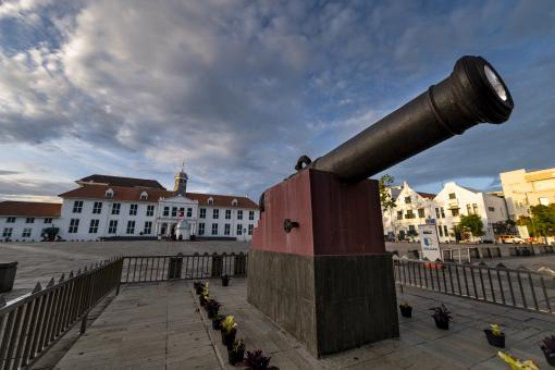 A large cannon displayed in a large square with buildings in the background, beneath a cloudy sky.